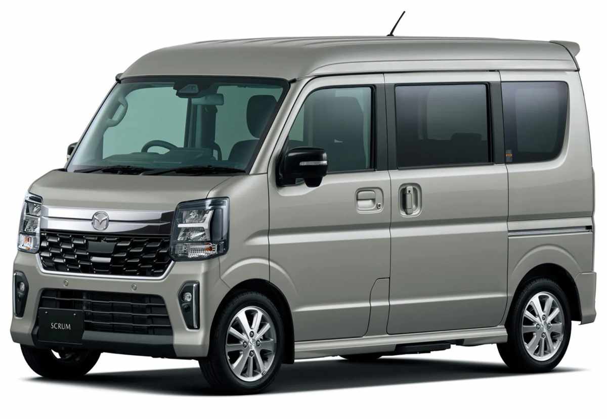 Perfil delantero tres cuartos de la Mazda Scrum Wagon para pasajeros en tono arena metalizado, resaltando su vistosa parrilla cromada, luces exploradoras en el bumper, faros oscurecidos y rines de aleación de diseño elegante.