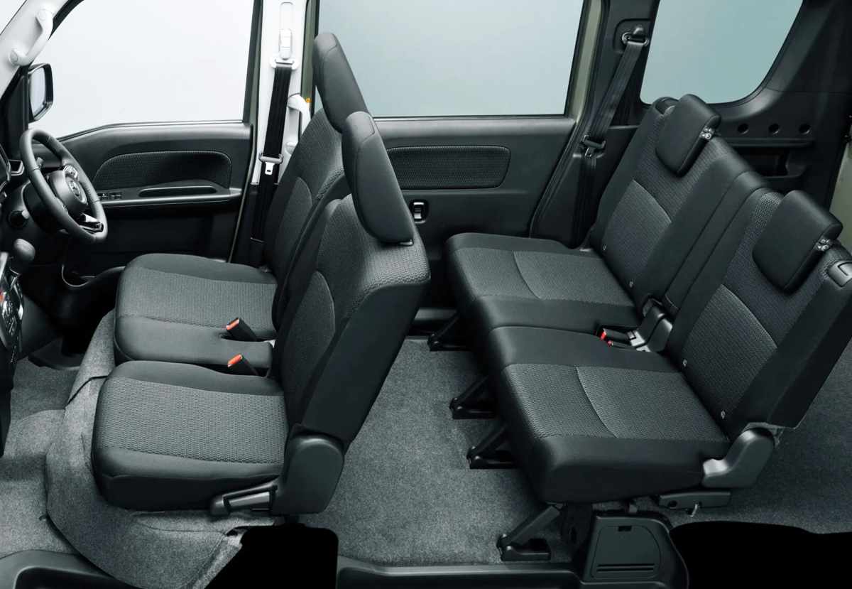 Habitáculo interior de la Mazda Scrum Wagon configurado para cuatro pasajeros, revelando los asientos tapizados en tela gris oscura con diseño independiente y el amplio espacio para las piernas gracias al suelo completamente plano.