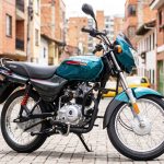 Motocicleta Bajaj Boxer CT100 ES Spoke color verde azulado estacionada sobre una calle adoquinada con edificios residenciales al fondo.