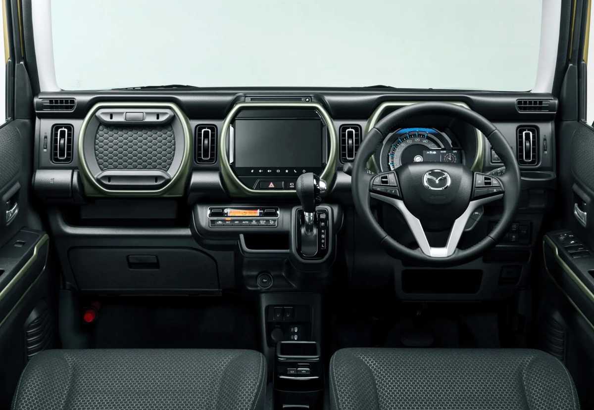 Tablero interior del Mazda Flair Crossover 2027, exhibiendo el volante multifuncional, la nueva pantalla central de 9 pulgadas y detalles de la consola en color caqui.