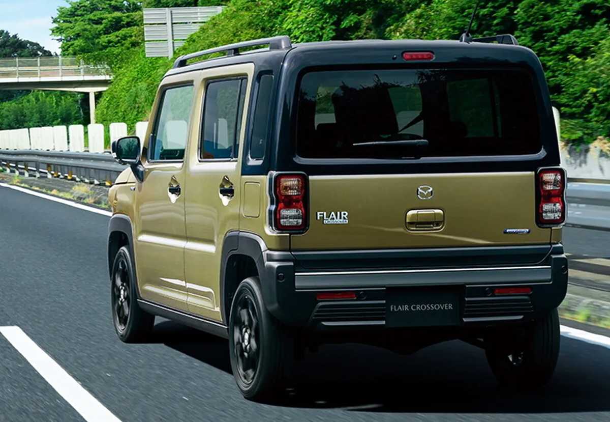 Mazda Flair Crossover versión aventurera color Khaki Bosque en movimiento por una autopista, visto desde su ángulo trasero derecho.