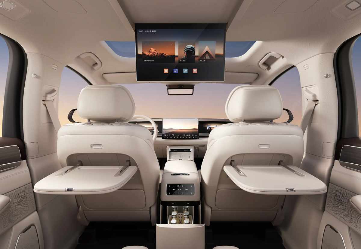Amplio habitáculo de la BYD Great Tang visto desde atrás, mostrando el techo panorámico, la pantalla multimedia trasera y mesas plegables tipo avión para los pasajeros.