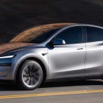 Crossover eléctrico Tesla Model Y color plata en movimiento sobre una carretera con líneas amarillas durante el día en Colombia.