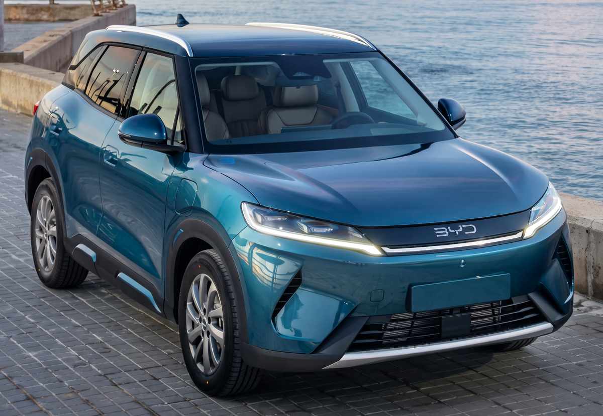Vista frontal en tres cuartos de la SUV BYD Yuan Up DM-i GS en color gris, estacionada en un muelle con el mar de fondo.