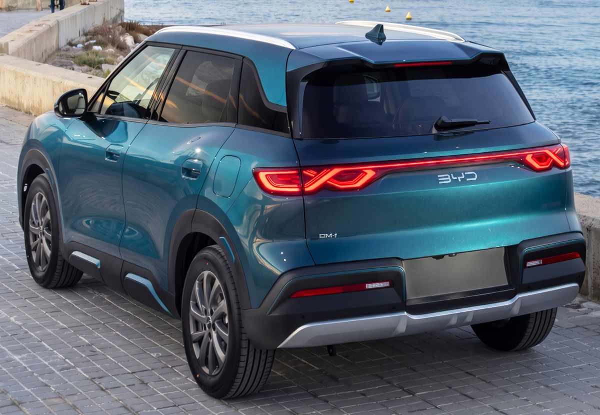 Vista trasera en tres cuartos de la SUV BYD Yuan Up DM-i GS color negro obsidiana, mostrando las luces traseras LED encendidas y estacionada en un muelle.