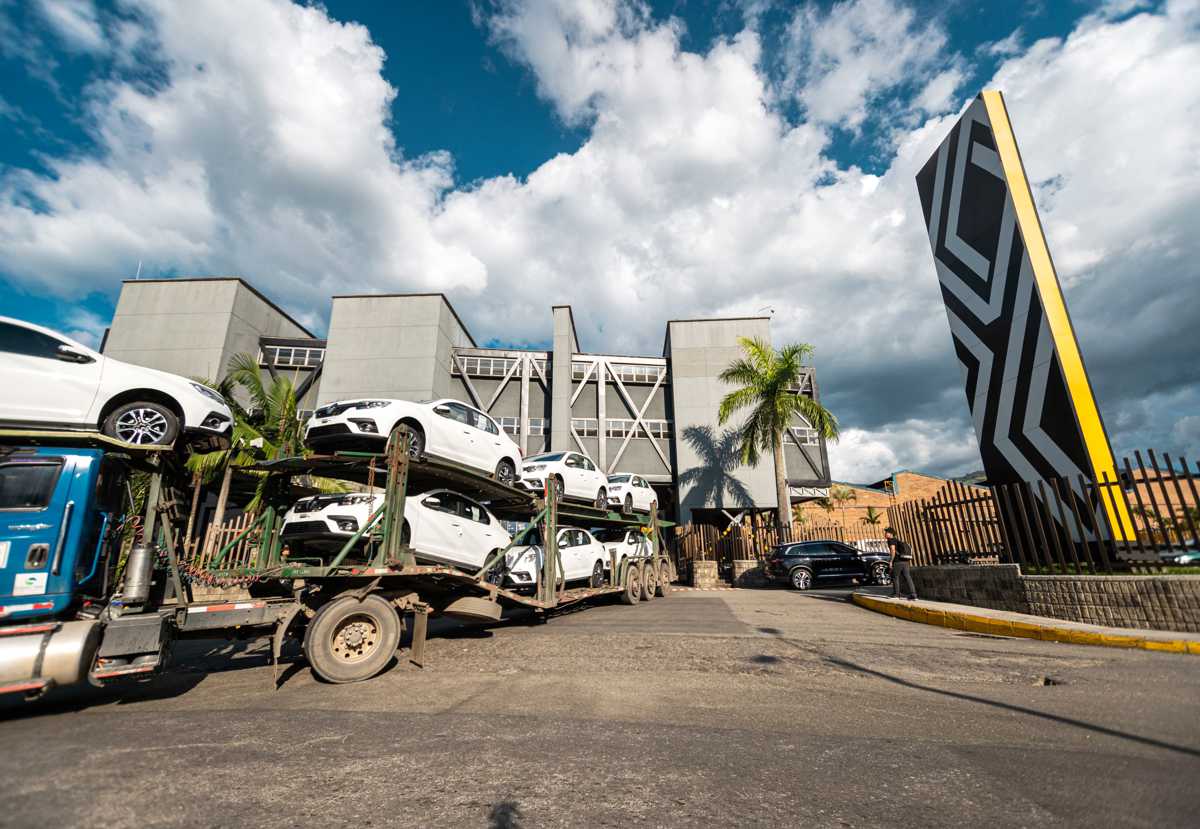 Camión tipo niñera cargado con varios vehículos Renault de color blanco saliendo por la entrada principal de la sede administrativa de Renault-Sofasa.