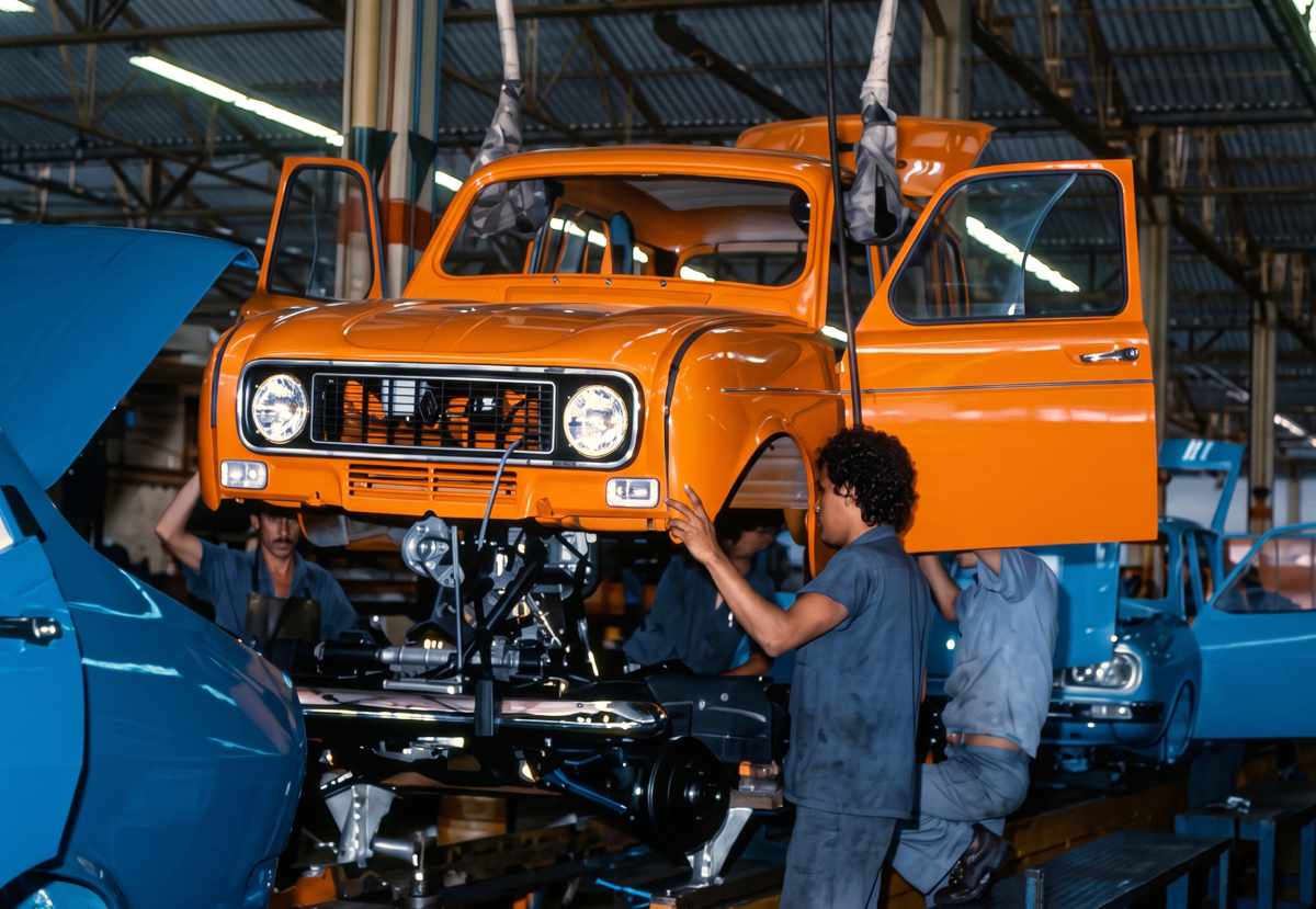 Operarios colombianos trabajando en el ensamblaje manual de la carrocería de un Renault 4 color naranja en las líneas de producción históricas de Sofasa.