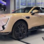 SUV eléctrica premium Avatr 11 de color beige exhibida en un moderno salón de ventas, mostrando su diseño aerodinámico, rines deportivos y cámaras laterales.