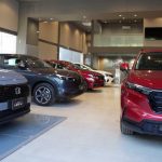 Interior de un concesionario Honda mostrando vehículos nuevos de exhibición, destacando una camioneta HR-V gris y una CR-V roja en primer plano.