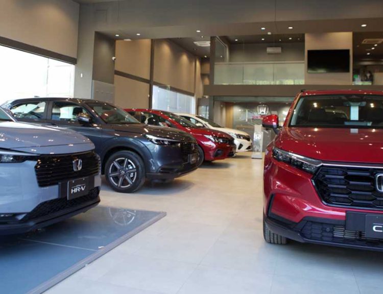 Interior de un concesionario Honda mostrando vehículos nuevos de exhibición, destacando una camioneta HR-V gris y una CR-V roja en primer plano.