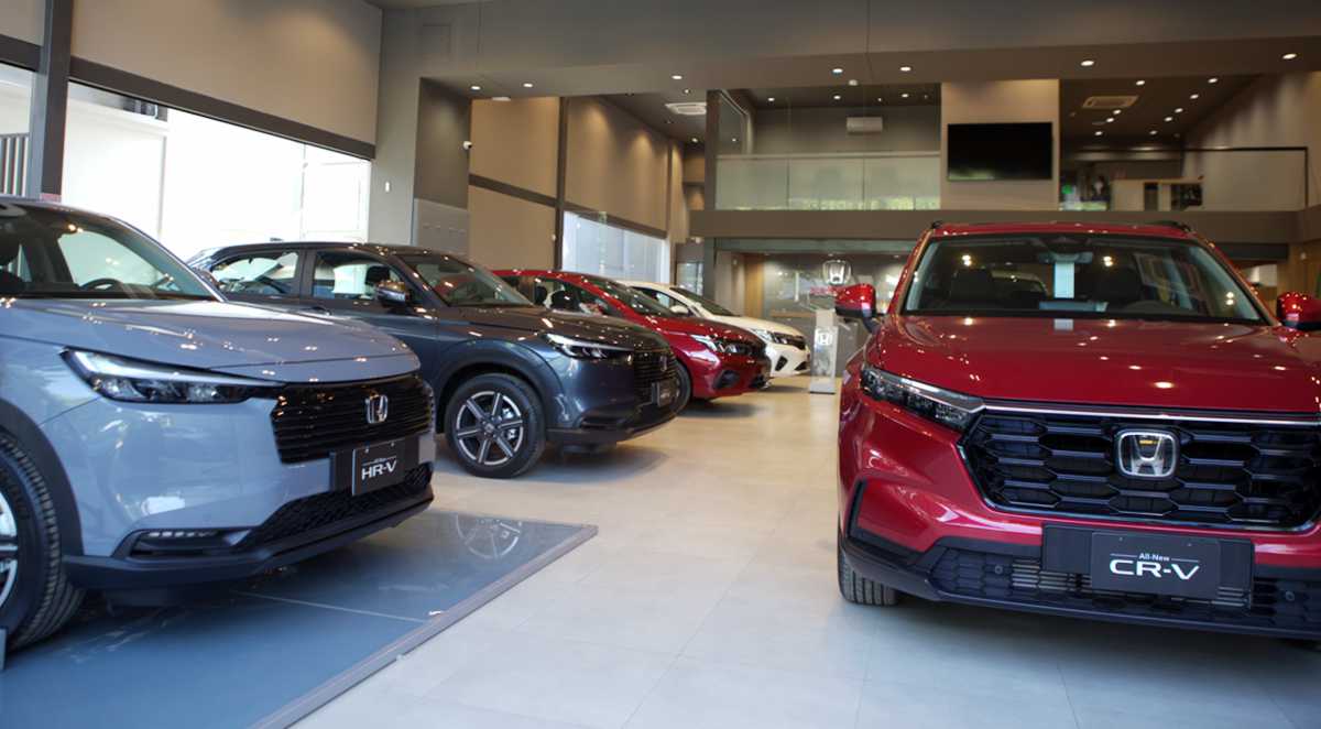 Interior de un concesionario Honda mostrando vehículos nuevos de exhibición, destacando una camioneta HR-V gris y una CR-V roja en primer plano.