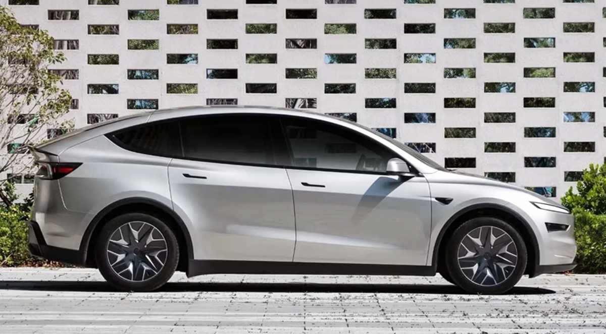 Vista lateral de perfil completo de la nueva Tesla Model Y L color plata en su variante extendida, estacionada frente a una pared geométrica blanca.
