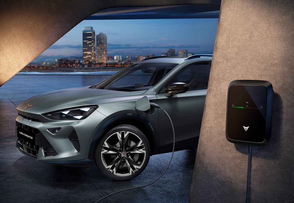La nueva Cupra Formentor PHEV conectada a un dispositivo de carga eléctrica domiciliaria en la pared, detallando el puerto de carga abierto en el guardabarros delantero.