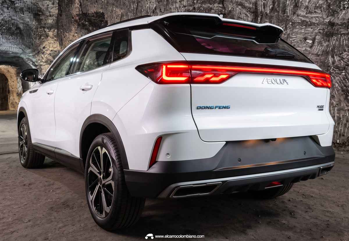 Vista trasera de tres cuartos de la SUV Dongfeng Huge blanca en el interior de una caverna, mostrando la barra de luz LED encendida de lado a lado.