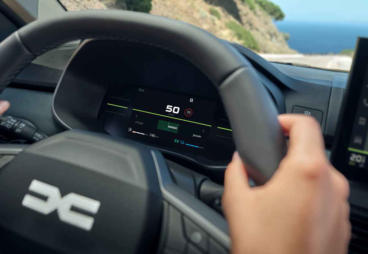 Perspectiva interior desde el volante del Dacia Sandero híbrido, enfocando el nuevo cuadro de instrumentos digital que muestra el indicador de velocidad y el modo de conducción eléctrica EV activado.