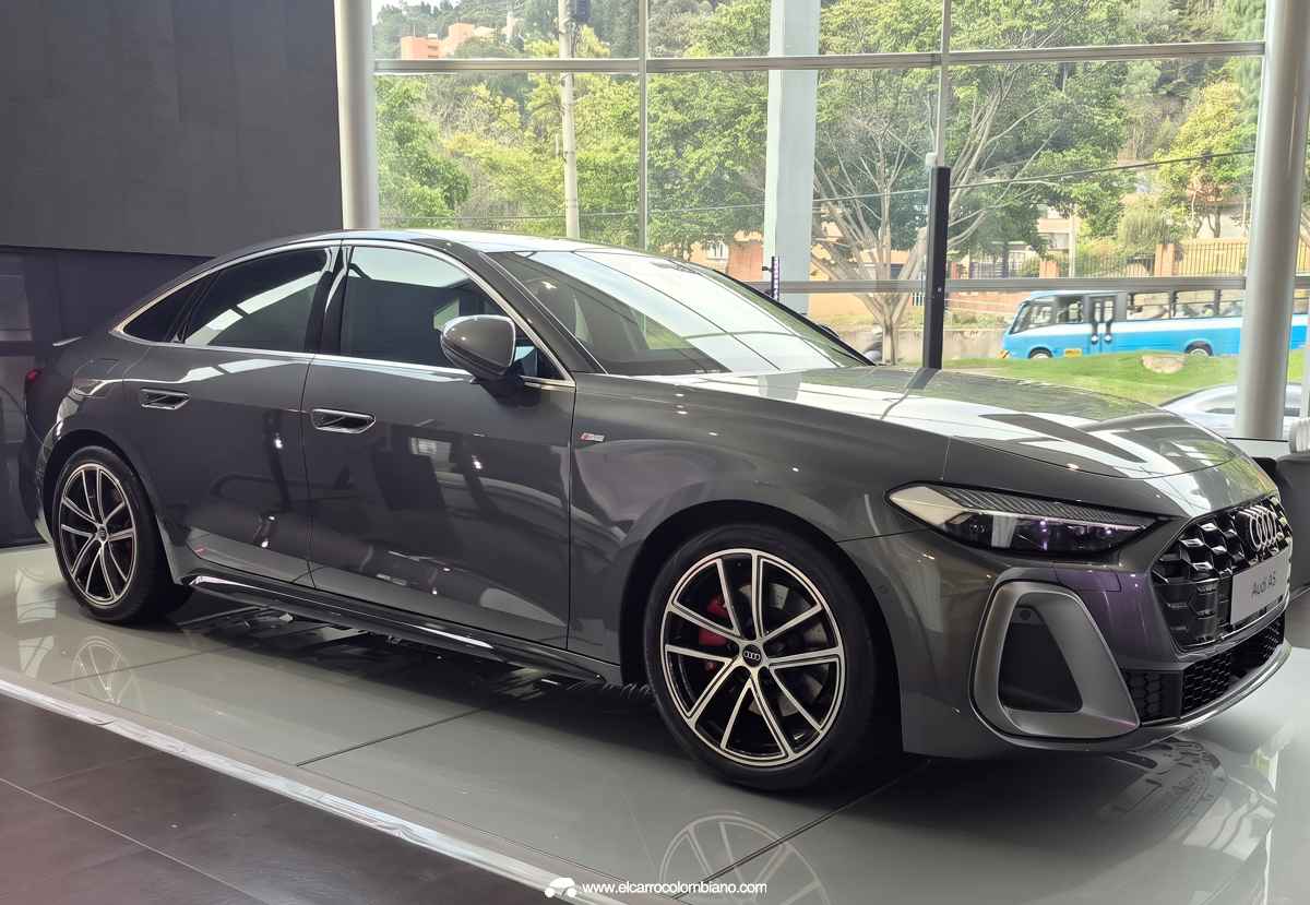 Plano delantero lateral del Audi A5 híbrido gris en concesionario, detallando sus faros Matrix LED más delgados y los faldones con moldura negra brillante.
