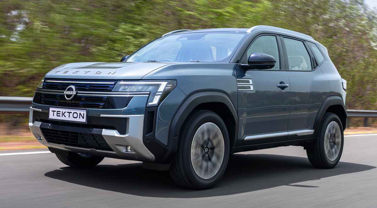 Vista frontal de tres cuartos de la nueva SUV Nissan Tekton color azul grisáceo en movimiento sobre una carretera, destacando su imponente parrilla frontal inspirada en la Nissan Patrol.