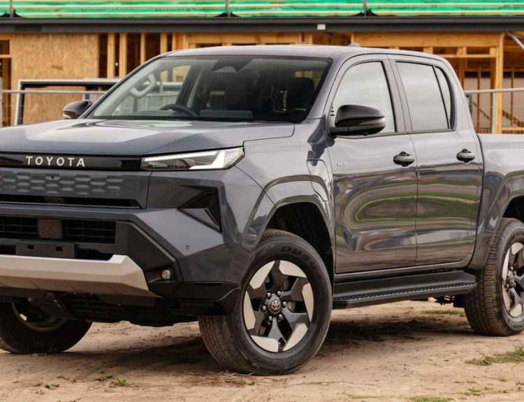 Vista frontal de tres cuartos de una Toyota Hilux color gris oscuro estacionada frente a una obra de construcción en madera, ilustrando su enfoque como pick-up para el trabajo duro.