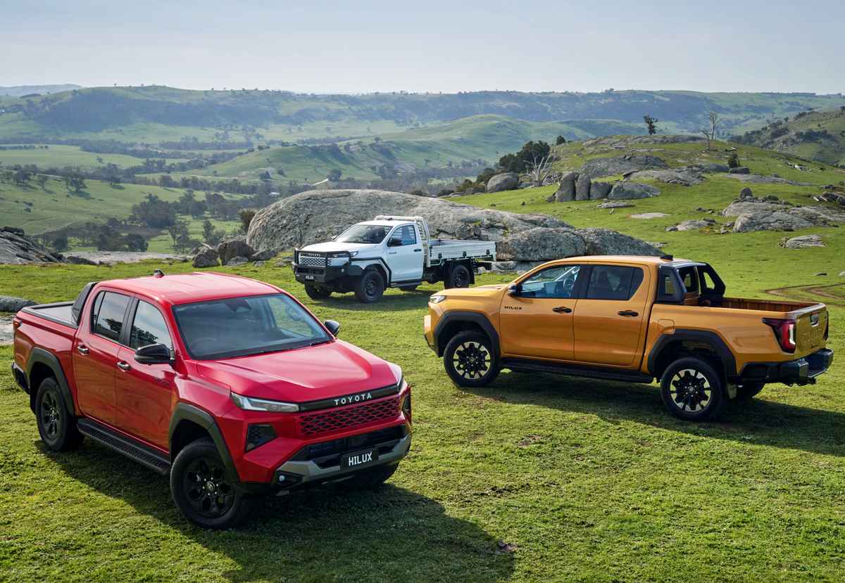 Tres camionetas Toyota Hilux de diferentes versiones y colores, incluyendo un modelo blanco de chasis cabina sencilla para trabajo, estacionadas en un entorno rural montañoso.