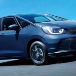 Vista frontal de tres cuartos del nuevo Honda Fit 2027 híbrido color azul oscuro en movimiento sobre una autopista, destacando su carrocería monovolumen y faros LED.