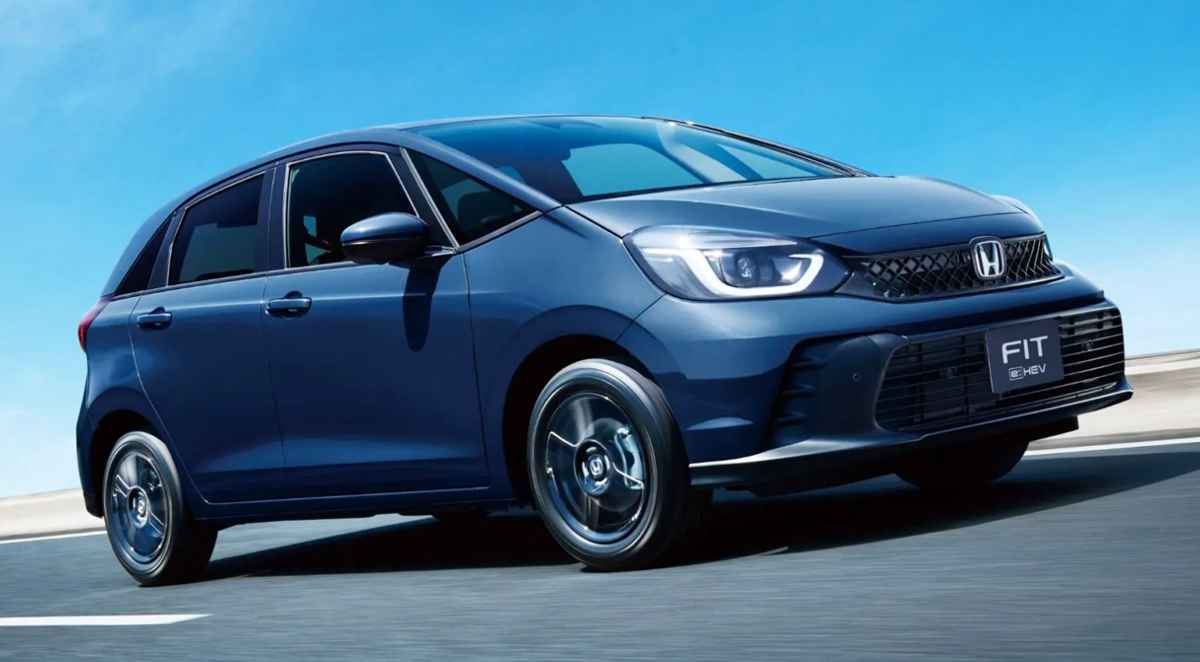Vista frontal de tres cuartos del nuevo Honda Fit 2027 híbrido color azul oscuro en movimiento sobre una autopista, destacando su carrocería monovolumen y faros LED.