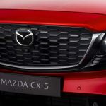 Detalle frontal cercano de la parrilla negra y el faro LED de la nueva Mazda CX-5 color rojo brillante, modelo que estrenará el primer sistema híbrido completo de la marca.