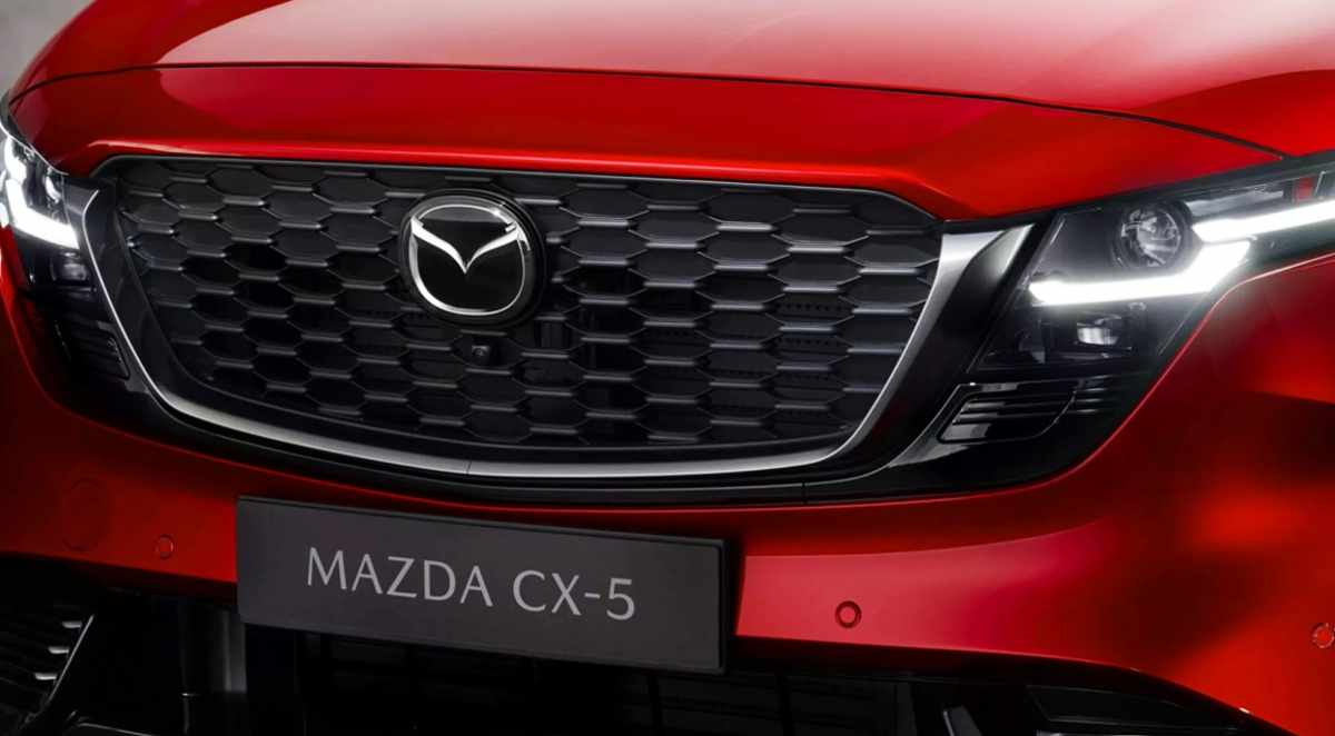 Detalle frontal cercano de la parrilla negra y el faro LED de la nueva Mazda CX-5 color rojo brillante, modelo que estrenará el primer sistema híbrido completo de la marca.