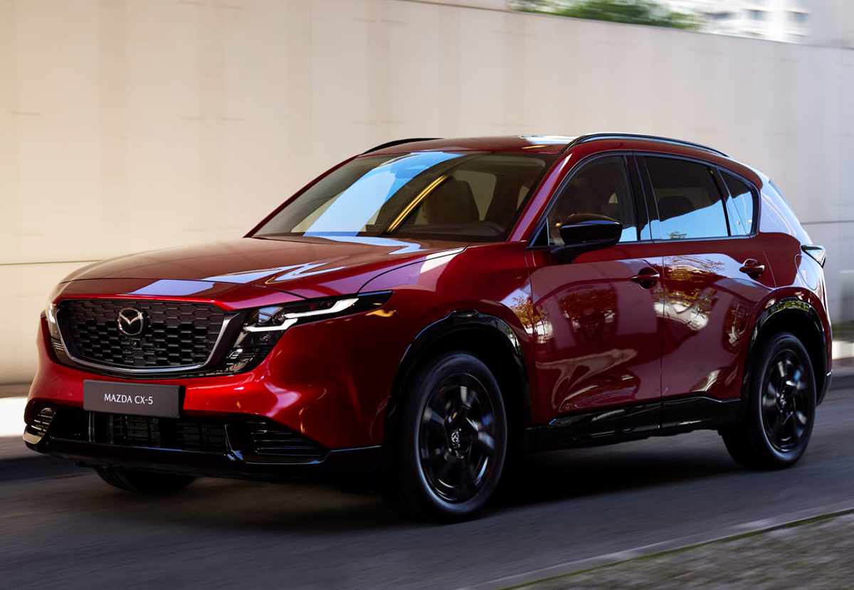 Vista frontal en movimiento de la nueva Mazda CX-5 color rojo brillante circulando con fluidez por la ciudad, destacando su elegante diseño Kodo, faros LED y vocación familiar.
