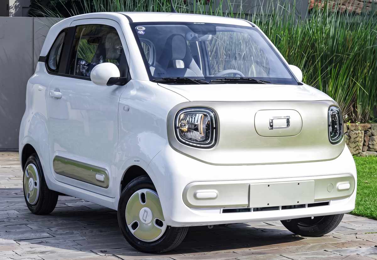 FAW Bestune Xiaoma, el carro nuevo más barato de Colombia, luciendo su carrocería compacta en color blanco con detalles pastel sobre un camino de piedra rodeado de naturaleza.
