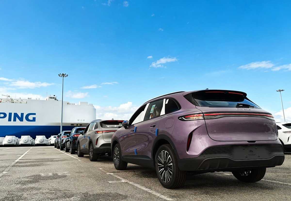 Fila de vehículos SUV de la marca Lepas L8 en distintos colores, estacionados en un puerto marítimo listos para ser embarcados en un gran buque carguero para su exportación.