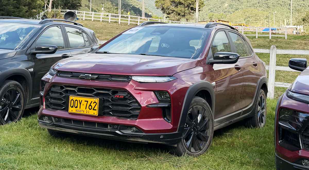 Vista frontal de tres cuartos del nuevo Chevrolet Sonic RS en color rojo, destacando su parrilla tipo panal y diseño crossover, estacionado sobre césped durante su prueba de ruta en Colombia.