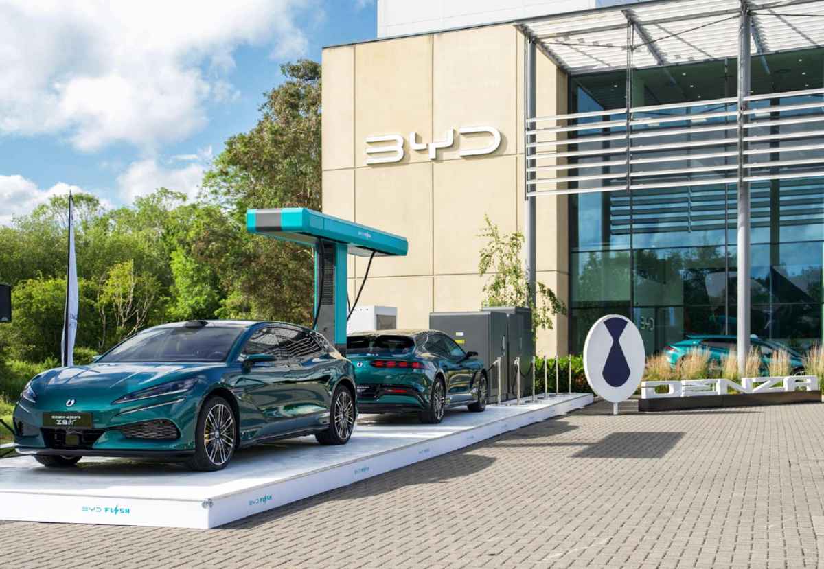 Estación de carga rápida de BYD en Europa con dos vehículos eléctricos de la submarca premium Denza recargando baterías, destacando su millonaria inversión en infraestructura propia.
