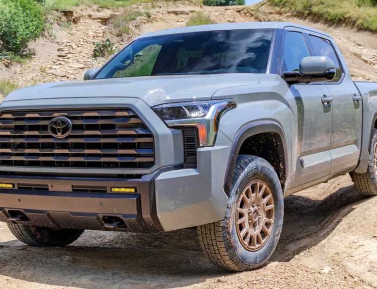 Vista frontal de tres cuartos de la nueva Toyota Tundra 2027 versión Trailhunter en color gris, exhibiendo su renovada parrilla hexagonal y rines bronce en un camino destapado.