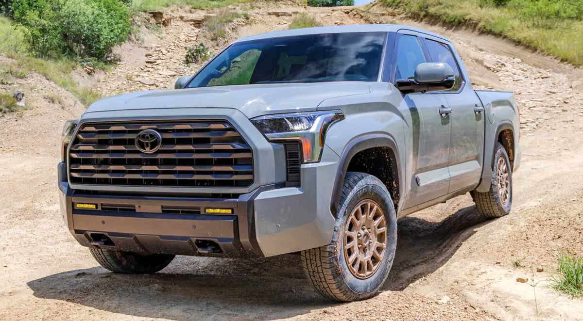 Vista frontal de tres cuartos de la nueva Toyota Tundra 2027 versión Trailhunter en color gris, exhibiendo su renovada parrilla hexagonal y rines bronce en un camino destapado.