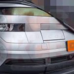 Foto espía frontal de la próxima generación de la Hyundai Kona parcialmente cubierta por una lona negra, revelando su nuevo faro geométrico y capó plano.