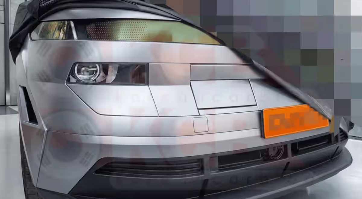 Foto espía frontal de la próxima generación de la Hyundai Kona parcialmente cubierta por una lona negra, revelando su nuevo faro geométrico y capó plano.