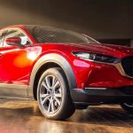 Vista frontal de tres cuartos de la Mazda CX-30 híbrida en color rojo brillante, exhibida bajo las luces de la vitrina del concesionario Madiautos Mazda.