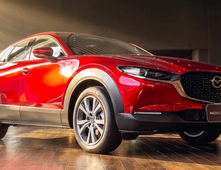 Vista frontal de tres cuartos de la Mazda CX-30 híbrida en color rojo brillante, exhibida bajo las luces de la vitrina del concesionario Madiautos Mazda.