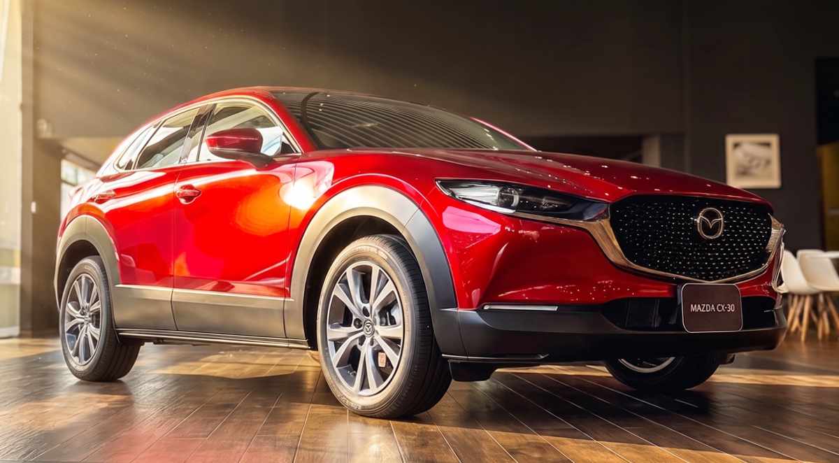 Vista frontal de tres cuartos de la Mazda CX-30 híbrida en color rojo brillante, exhibida bajo las luces de la vitrina del concesionario Madiautos Mazda.