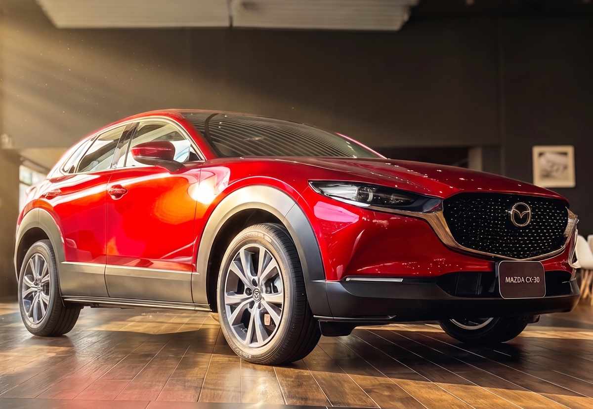Vista frontal de tres cuartos de la Mazda CX-30 híbrida en color rojo brillante, exhibida bajo las luces de la vitrina del concesionario Madiautos Mazda.