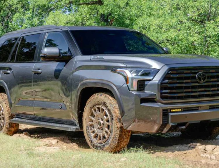 Vista frontal de tres cuartos de la nueva Toyota Sequoia 2027 versión Trailhunter en color gris oscuro, superando un terreno embarrado.