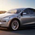 Vehículo eléctrico Tesla Model Y color plata en movimiento por una carretera al atardecer, destacando como el carro más vendido de Colombia en 2026.