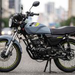 Motocicleta AKT AK125 NKD de color gris con detalles amarillos estacionada en una calle urbana, destacándose como la moto más vendida de Colombia en el primer semestre del 2026.