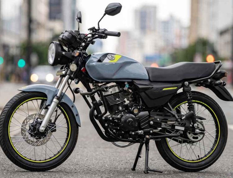 Motocicleta AKT AK125 NKD de color gris con detalles amarillos estacionada en una calle urbana, destacándose como la moto más vendida de Colombia en el primer semestre del 2026.