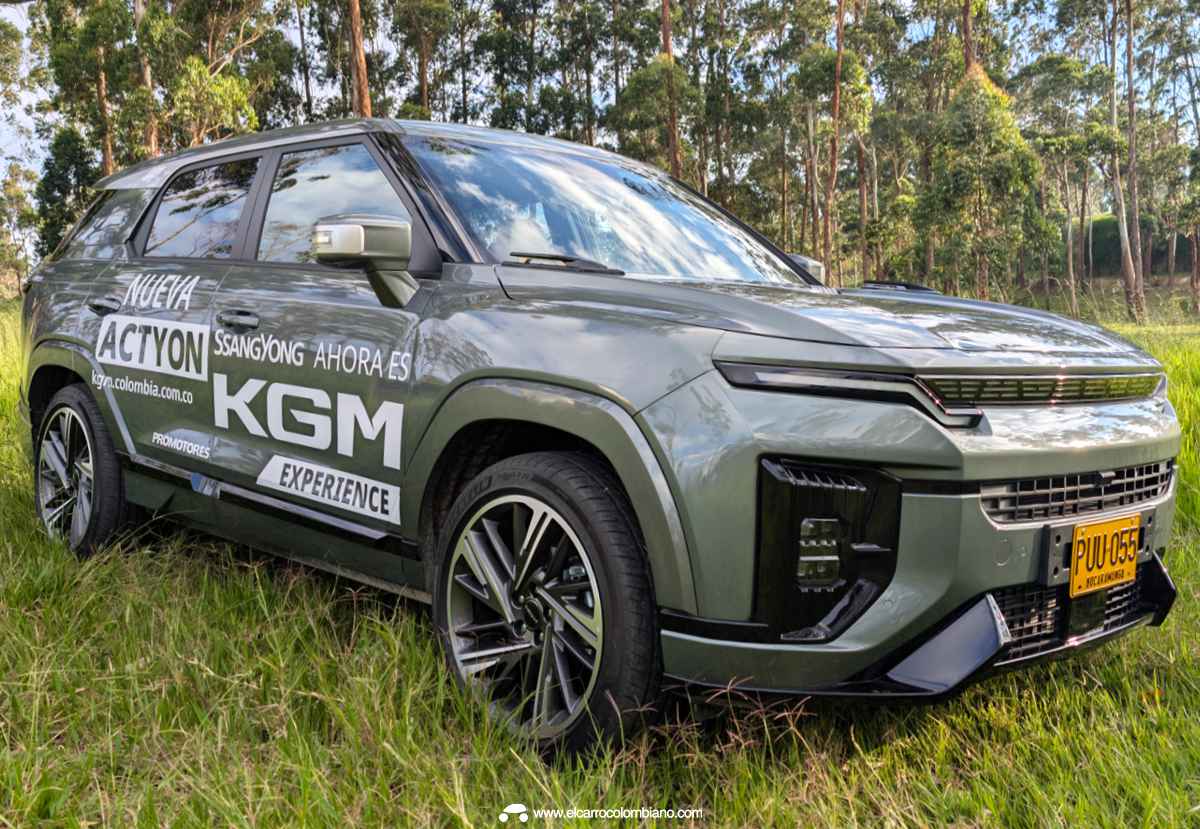 Vista frontal de tres cuartos de la SUV KGM Actyon color verde oliva sobre una zona verde, mostrando su diseño aerodinámico y parrilla iluminada sin el logo tradicional.