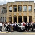 Numeroso grupo de estudiantes y directivos posando junto al Renault Kwid gris donado por Sofasa, frente a la imponente fachada de la Facultad de Minas de la Universidad Nacional.