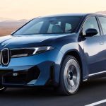 Vista frontal en movimiento de la nueva SUV BMW iX3 eléctrica color azul, destacando su renovada parrilla iluminada y diseño aerodinámico sobre una carretera despejada.