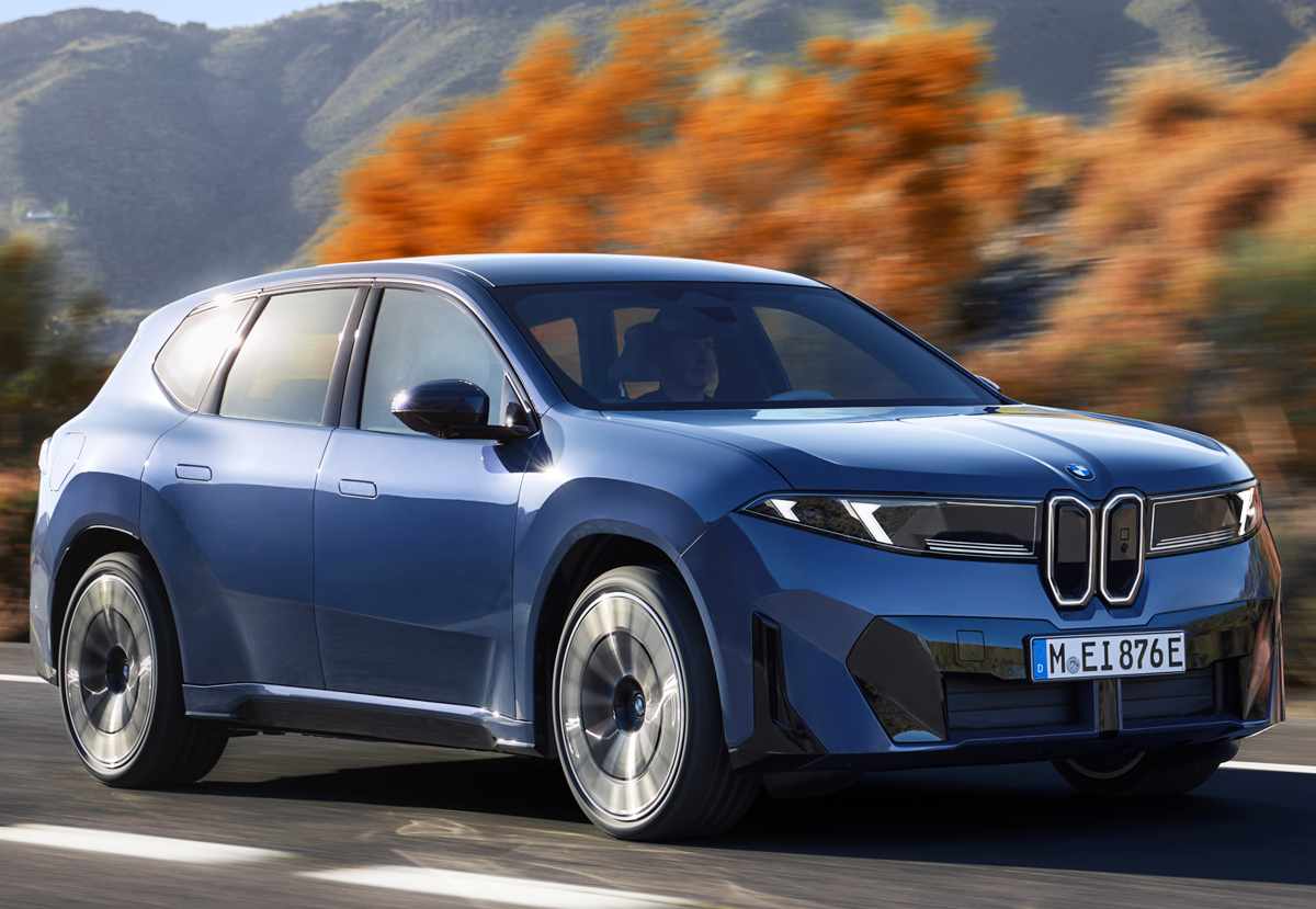 Perfil dinámico de tres cuartos de la BMW iX3 eléctrica azul rodando por una vía boscosa, mostrando sus rines M Sport bitono y líneas laterales minimalistas.
