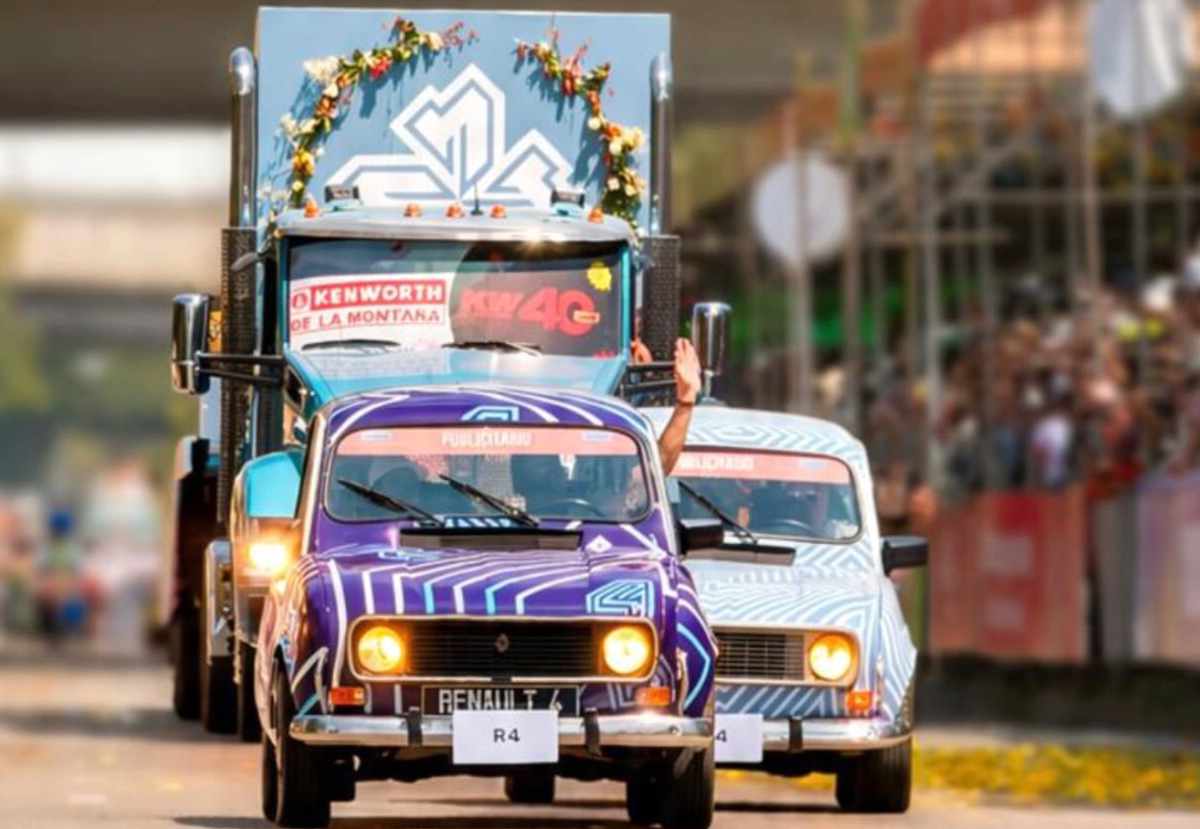 Dos clásicos vehículos Renault 4 con llamativos gráficos morados y blancos liderando la caravana oficial frente al imponente camión del nuevo modelo eléctrico.