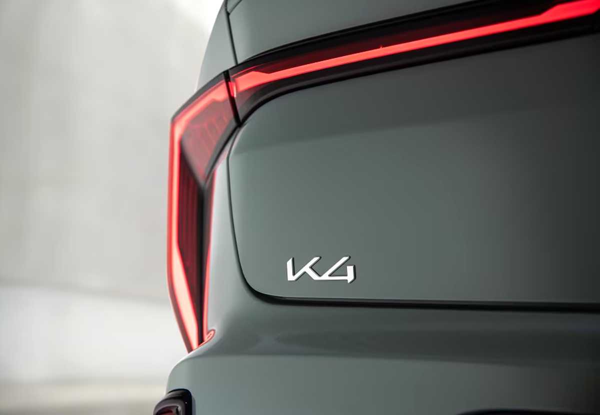 Toma macro de la compuerta trasera del sedán Kia K4, enfocándose en la elegante tipografía del emblema del modelo y el borde iluminado en rojo de sus luces traseras.